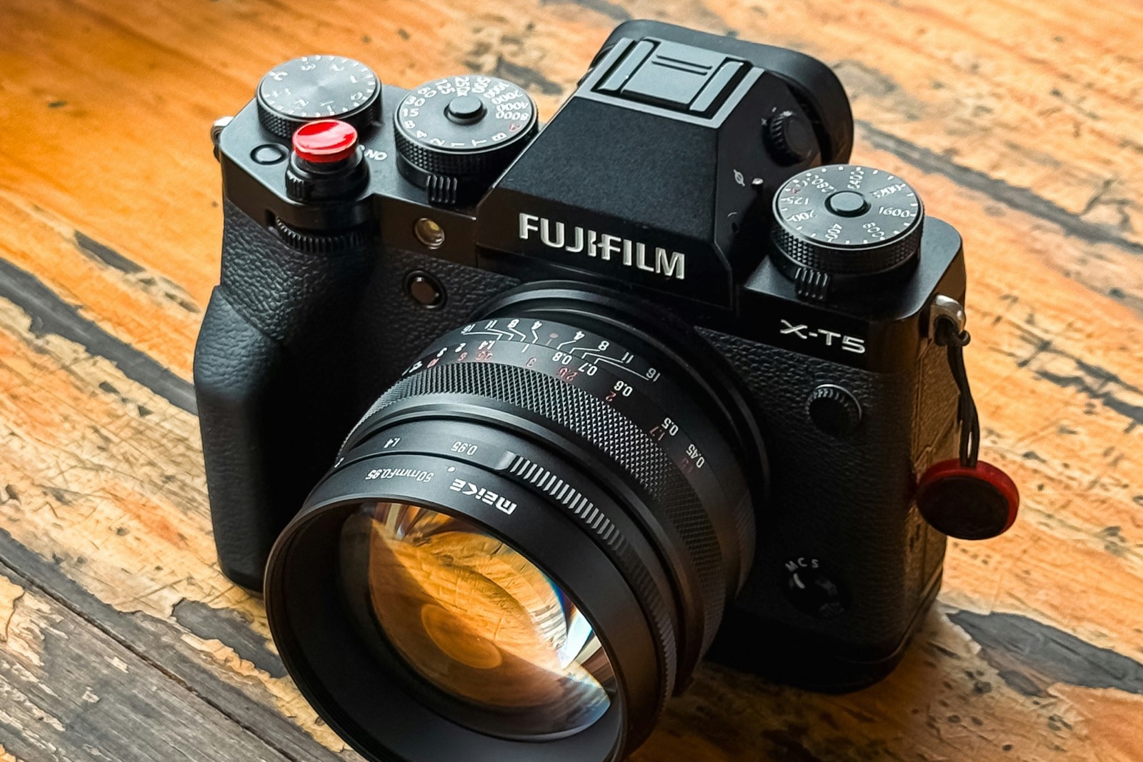A black Fujifilm X-T5 with a manual 50mm lens on a weathered wooden table