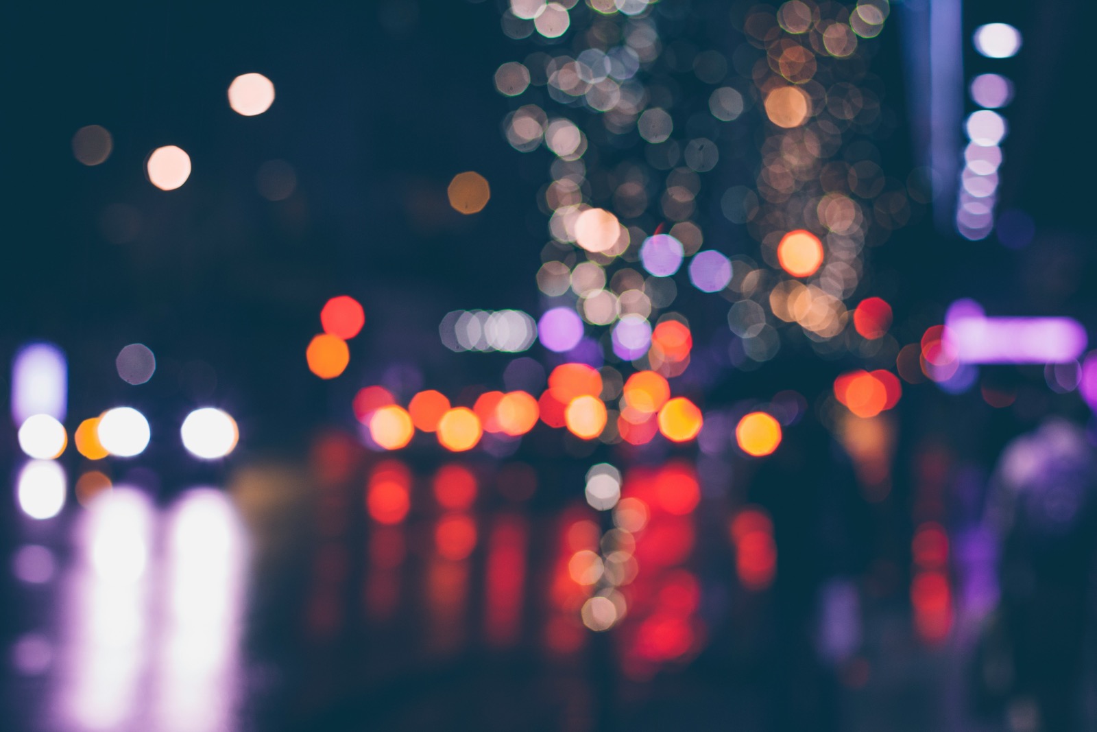 Out-of-focus city street at night with glowing orange, red and violet bokeh from street lights and car headlights