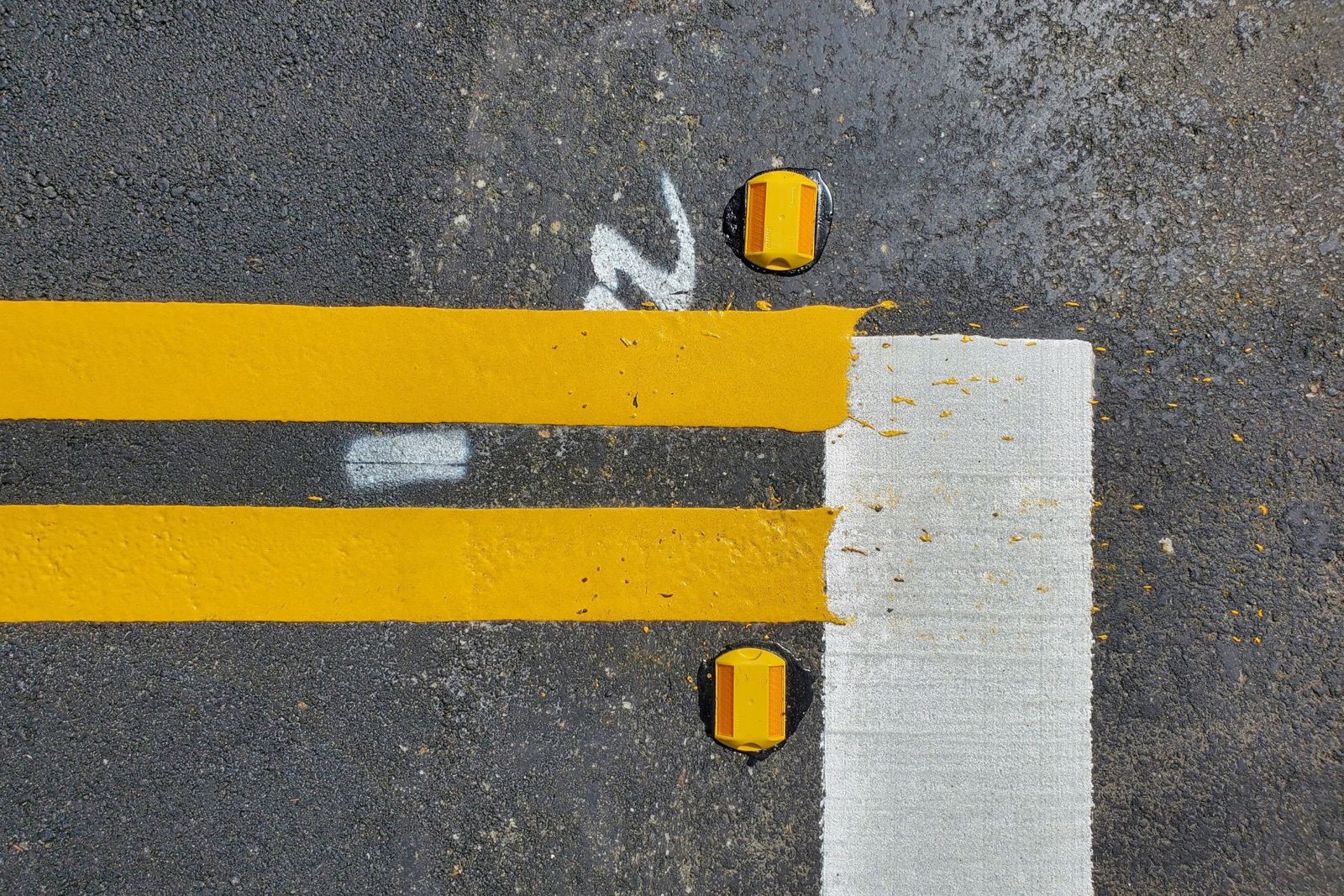 Freshly painted double yellow road lines and reflective markers on dark gray asphalt next to a white crosswalk stripe