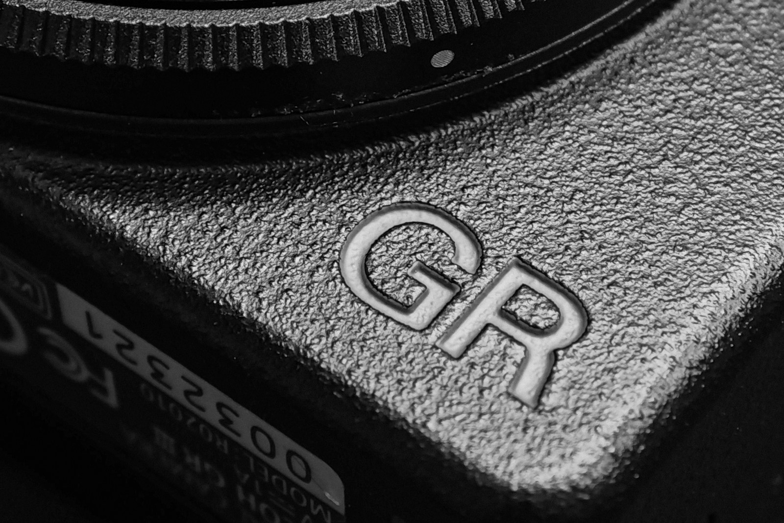 Black and white close-up of the textured grip and embossed GR logo on a Ricoh GR camera